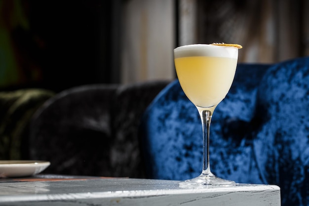 Glass with yellow lemon cocktail decorated with dried lemon chips on the blurred bar counter background