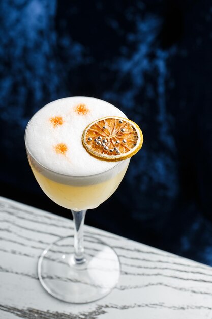 Glass with yellow lemon cocktail decorated with dried lemon chips on the blurred bar counter background