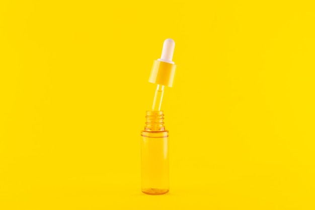 Glass yellow bottle with pipette with essential oil on yellow background top view Aromatic cosmetic