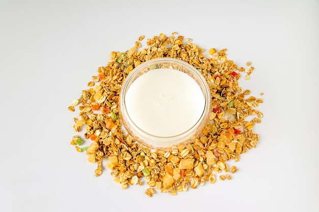 A glass of yogurt stands in a scattering of granola on a white background