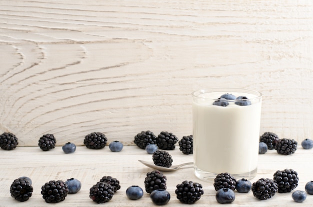 Glass of yogurt with berries, blueberries, blackberries and blueberries on the edge, light background