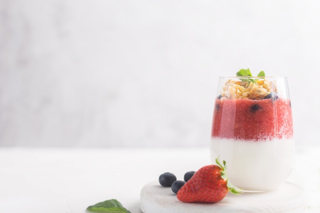 Bicchiere di yogurt con mousse di fragole, mirtilli e muesli su uno sfondo bianco