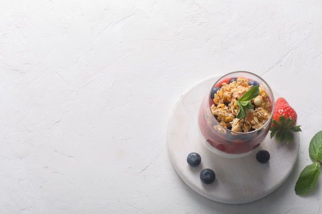 Glass of yogurt with strawberry mousse, blueberries and granola on a white background