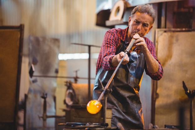 Photo glassblower shaping a glass on the blowpipe