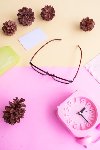 Glasses, alarm clock, pine tree flowers on a pastel pink and pastel yellow background. Summer Concept, Minimal Concept