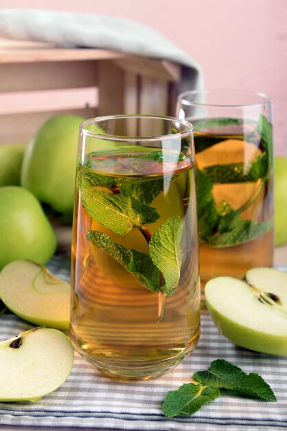 Glasses of apple juice with fruits and fresh mint on table close up