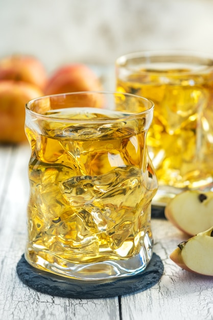 Glasses of Apple juice with ice and fresh red apple on a wooden table in a summer day.