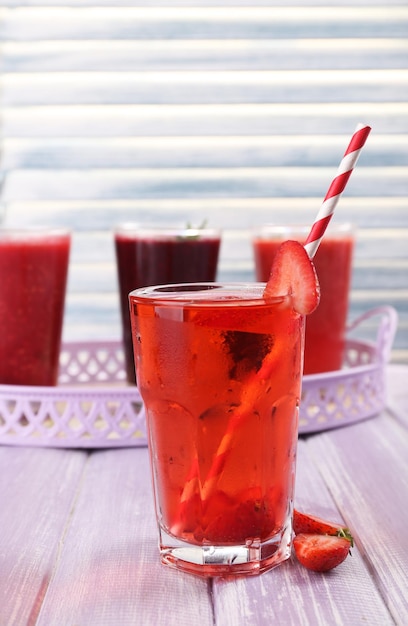 Glasses of berry cocktails on tray and on wooden surface on light background