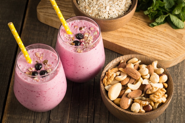 Glasses of berry smoothie with nuts, mint, blueberry, raspberry, and yogurt on wooden table. Weight loss and diet .