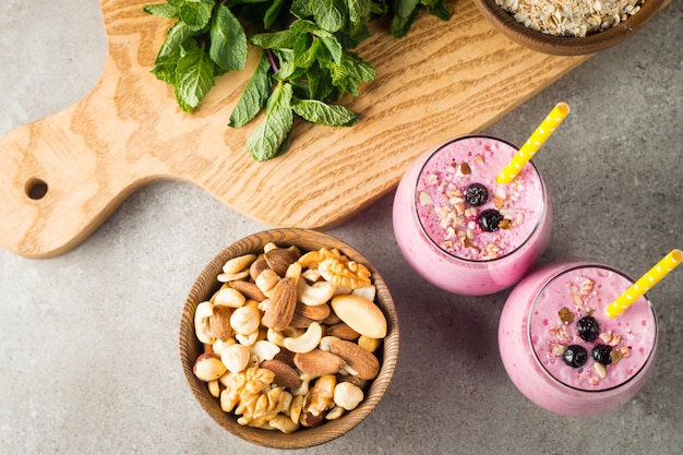 Glasses of berry smoothie with nuts, mint, blueberry, raspberry, and yogurt on wooden table. Weight loss and diet .