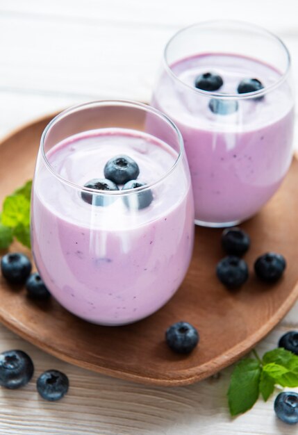 Glasses of blueberry yogurt with blueberries on a wooden background.