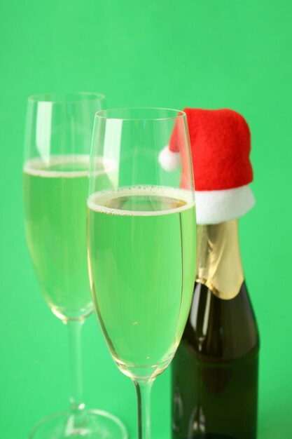 Glasses and bottle of champagne, and santa hat on green background