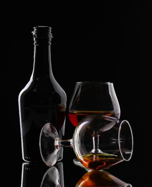 Glasses of brandy and bottle on black background