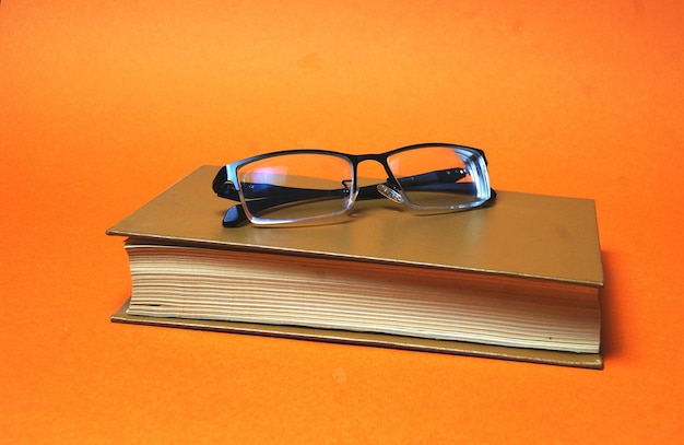 Очки на коричневой книге на ярко-оранжевом фоне