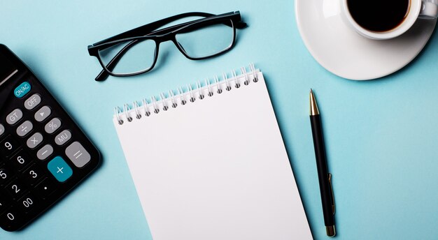 glasses, calculator, blank notebook and pen on a light blue. copy space