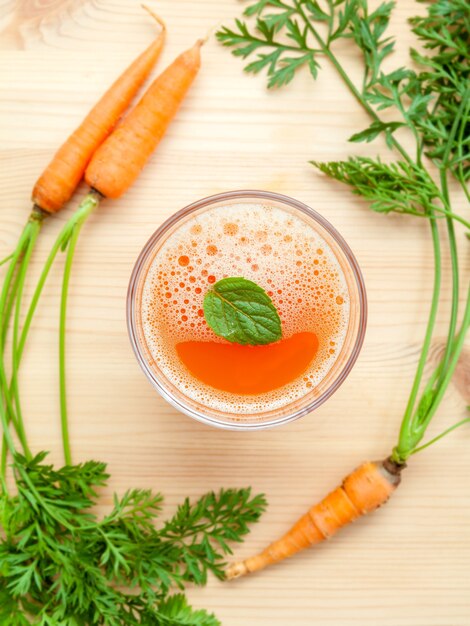 Photo glasses of carrot juice with carrot roots on wooden background.