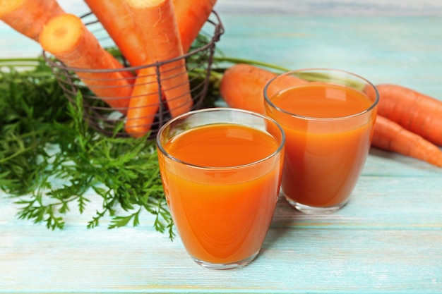 Glasses of carrot juice with vegetables on wooden background