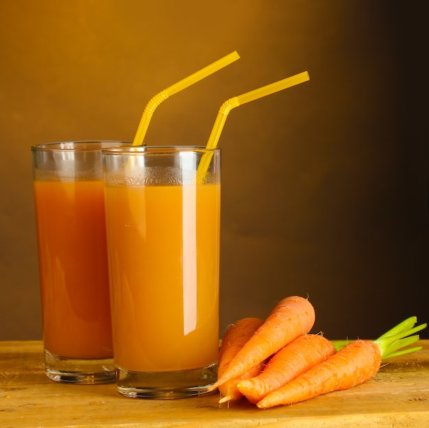 Foto bicchieri di succo di carota sulla tavola di legno su colore marrone