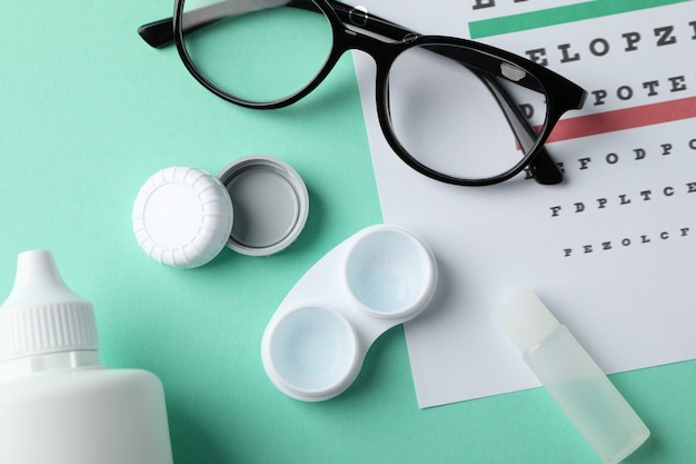 Glasses, case for contact lenses and eye test chart on mint surface, top view