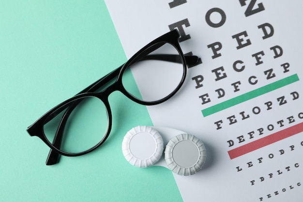 Glasses, case for contact lenses and eye test chart on mint surface, top view