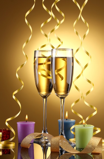 Glasses of champagne, candles, gifts and streamer on yellow background