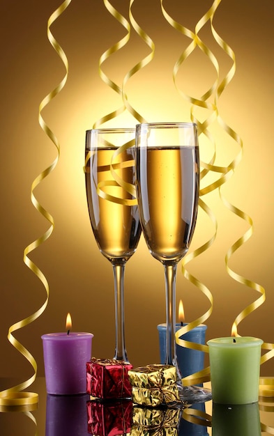 Glasses of champagne, candles, gifts and streamer on yellow background