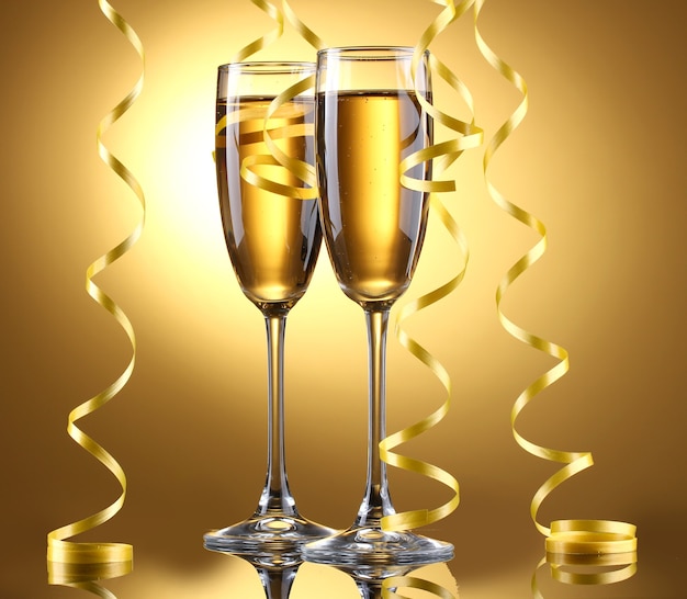 Glasses of champagne and streamer on yellow background