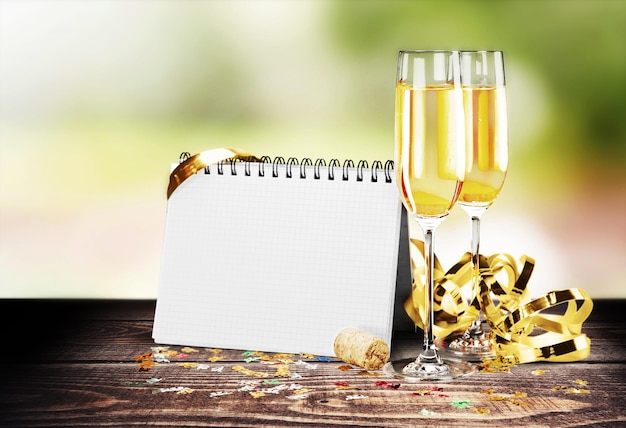 Glasses of champagne with curly ribbon and notepad on wooden table