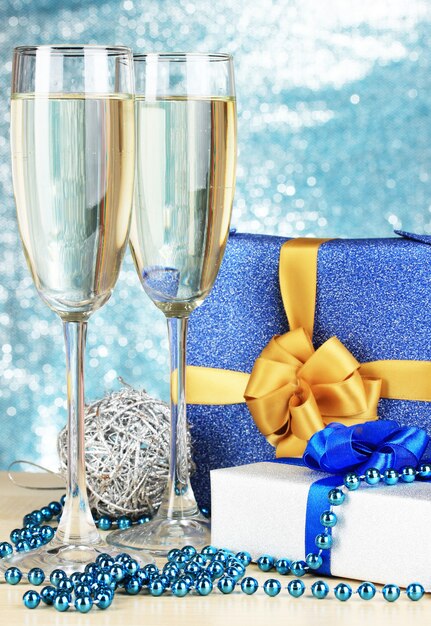 Glasses of champagne with gift boxes on shiny background