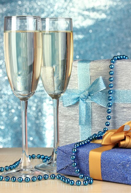 Glasses of champagne with gift boxes on shiny wall