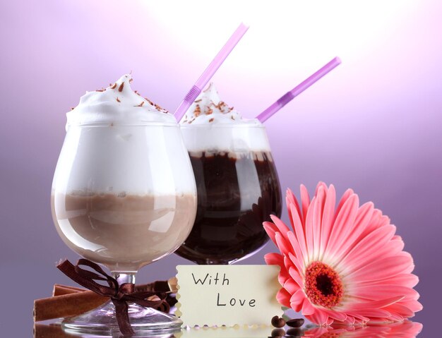 Glasses of coffee cocktail and gerbera flower on violet background