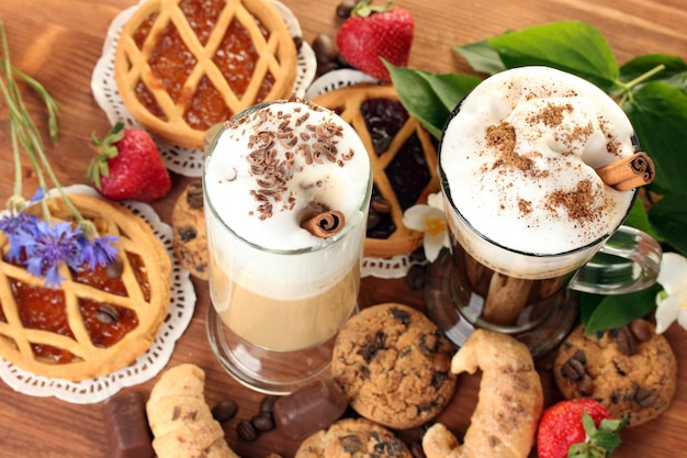 Photo glasses of coffee cocktail on wooden table with sweet and flowers