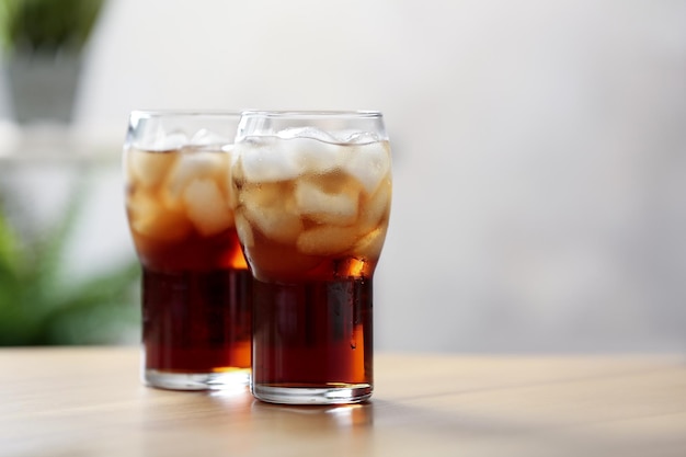 Glasses of cola with ice on table against blurred background space for text