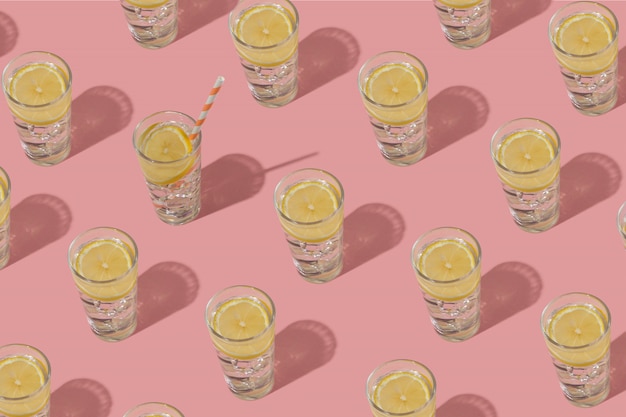 Glasses of cold water with ice and lemon. Repeating pattern on a pink background.