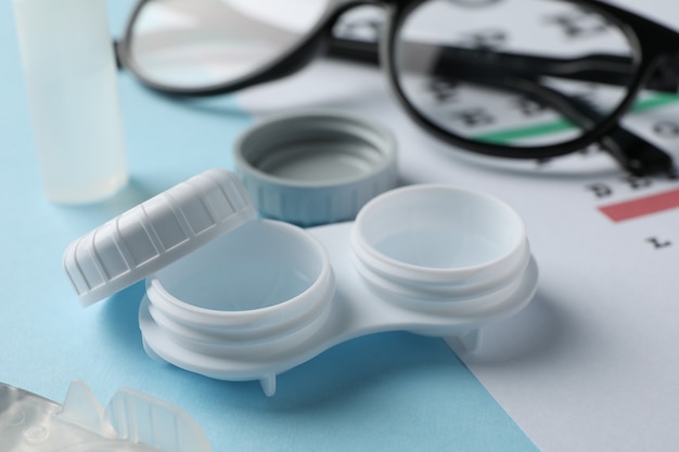 Glasses, contact lenses and eye test chart on blue surface, close up