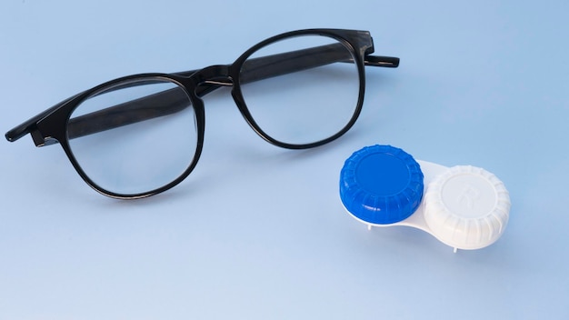 Glasses and container for contact lenses on a light blue background