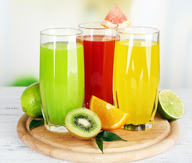 Glasses of different juice with fruits and mint on bright background