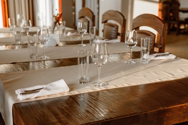 Glasses, flower fork, knife served for dinner in restaurant with cozy interior. Empty glasses in restaurant