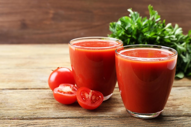 Glasses of fresh tomato juice on wooden background