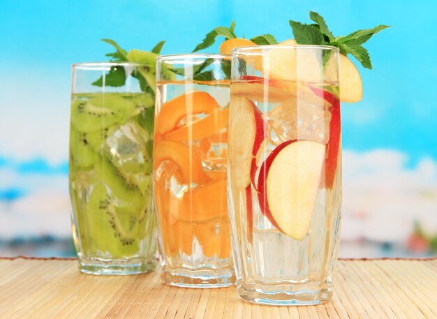 Glasses of fruit drinks with ice cubes on blue background