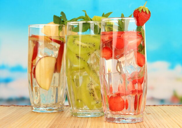 Glasses of fruit drinks with ice cubes on blue background