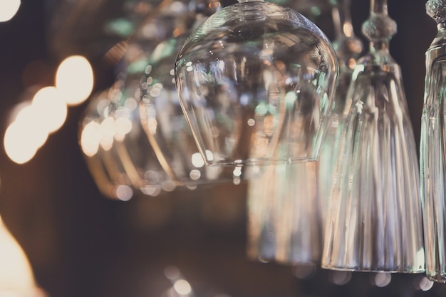 Glasses hanging on bar rack close up. Clean utensil for wine and cognac in restaurant, barroom background