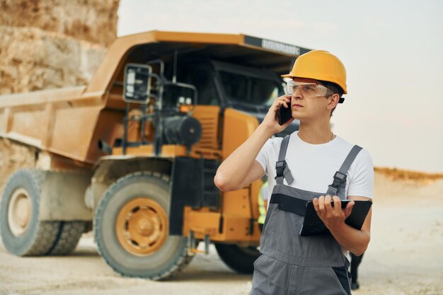 In glasses and hard hat worker in professional uniform is on\
the borrow pit at daytime