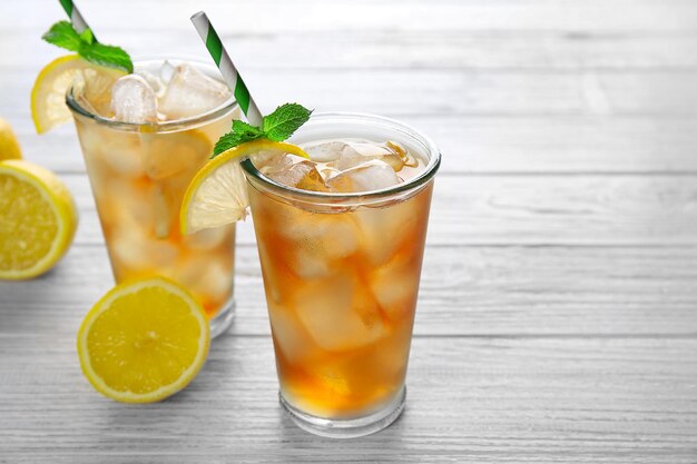 Стаканы чая со льдом с ломтиками лимона и мятой на белом деревянном фоне