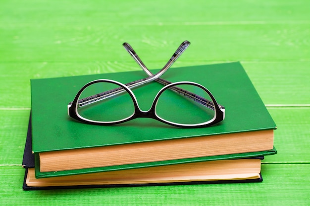 Glasses lie on two hardcover books on a green wooden table