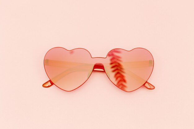 Occhiali su sfondo rosa chiaro occhiali da sole moderni rossi e riflesso della foglia di palma