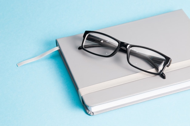 glasses and notebook on blue background copy space