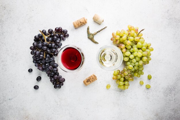 Фото Бокалы белого и красного вина со спелым виноградом на каменном фоне, вид сверху
