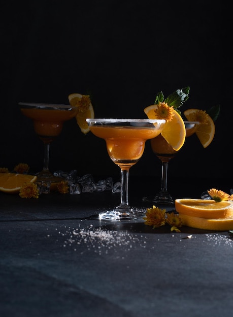 Glasses of orange cocktail decorated with orange and sugar on the edge of glass on black background