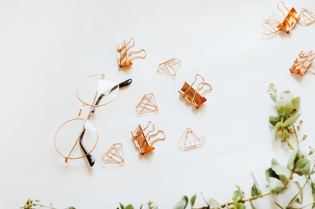 Glasses paper clips and clips in the form of rose gold diamonds on a background with green plants